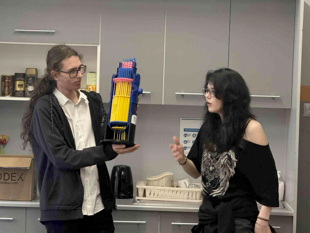 Kamil Kaczyński trzyma reaktor. Oliwia Fink z prawej strony tłumaczy jego działanie.